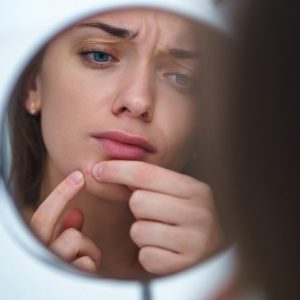 Sad woman looking at mirror and squeezing her acne