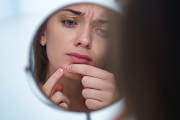 Sad woman looking at mirror and squeezing her acne