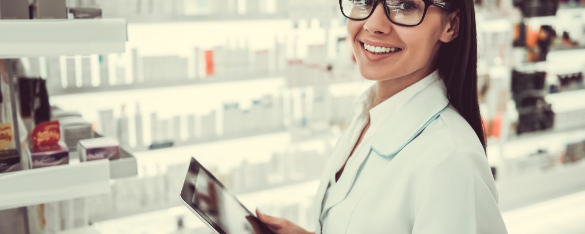 Female pharmacist using a digital tablet, looking at camera and smiling while working in pharmacy