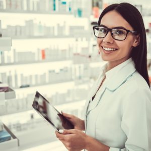 Female pharmacist using a digital tablet, looking at camera and smiling while working in pharmacy