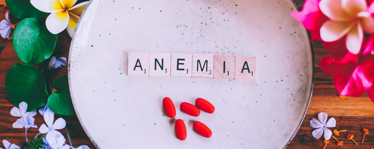 Wooden cubes with text Anemia on a plate with red iron tablets on a wooden table, with flowers in the background