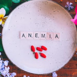 Wooden cubes with text Anemia on a plate with red iron tablets on a wooden table, with flowers in the background
