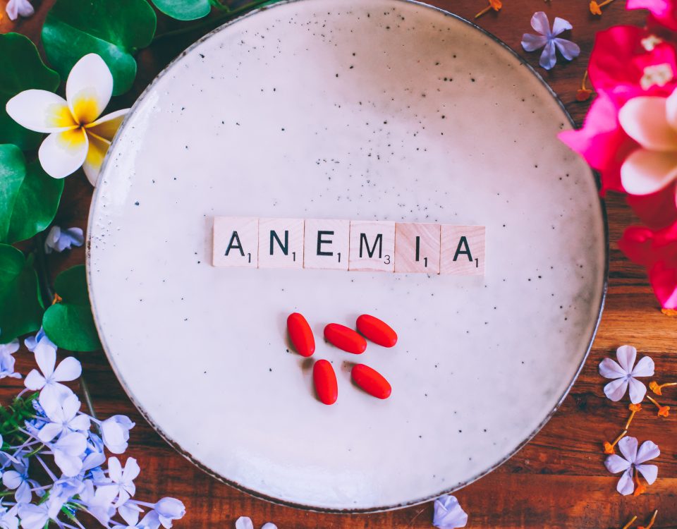 Wooden cubes with text Anemia on a plate with red iron tablets on a wooden table, with flowers in the background