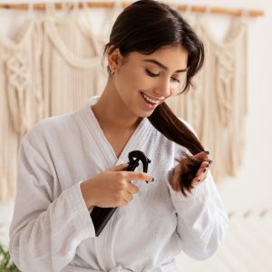 Lady Spraying Hair product on her hair in Bathroom representing hair care concept