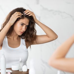 Unhappy Woman wearing white shirt Looking at Hair Flakes and dandruff at Mirror in Modern Bathroom