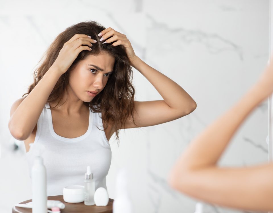 Unhappy Woman wearing white shirt Looking at Hair Flakes and dandruff at Mirror in Modern Bathroom