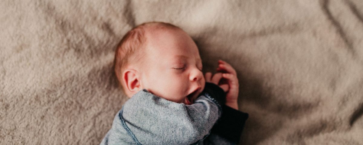 Newborn suffering from jaundice yawns while sleeping on brown blanket