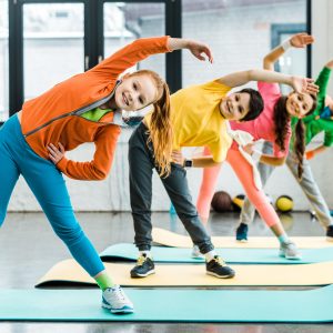 Group of smiling preteen kids wearing bright outfits and doing sport exercise together in a fitness class