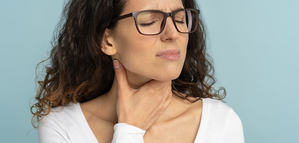 Sick woman wearing white blouse having sore throat on baby blue background