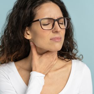 Sick woman wearing white blouse having sore throat on baby blue background
